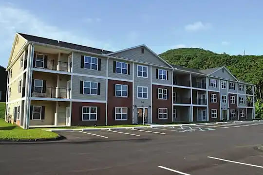 Modern apartment building with a freshly paved and striped parking lot in Dewart, Pennsylvania, with tree-covered hills in the background