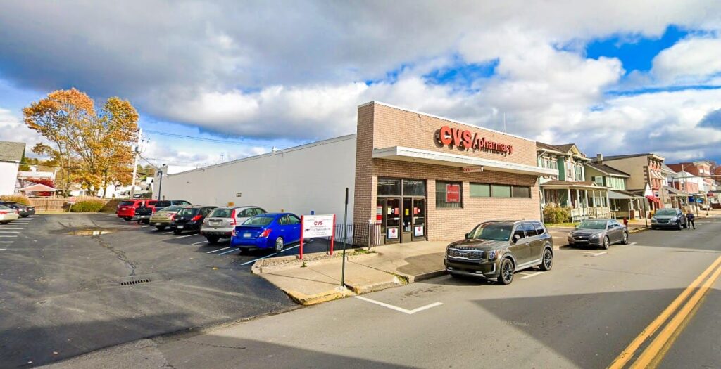 CVS Pharmacy storefront with adjacent parking lot and lined spaces in downtown Watsontown, Pennsylvania on a partly cloudy day