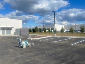 Newly paved commercial parking lot with fresh line striping equipment on site and retail buildings in the background.