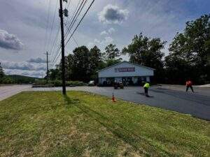 Fresh asphalt paving completed during summer at a commercial property, with crews smoothing and compacting the new pavement surface.