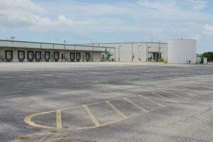 Large industrial asphalt lot serving a warehouse and distribution facility, featuring loading docks, truck access areas, and expansive pavement designed to support heavy commercial traffic and logistics operations.