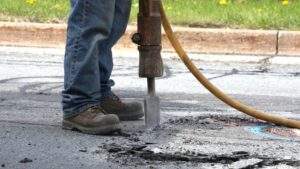 Construction worker breaking up cracked asphalt with a pneumatic jackhammer during fall pavement repairs